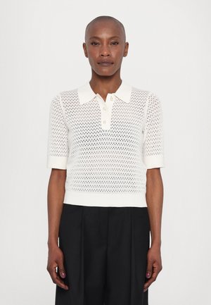 Pletený polo top v off-white barvě s texturovaným, perforovaným vzorem, krátkými rukávy a knoflíkovou légou; nošený s volnými černými kalhotami.