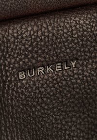 Braunes strukturiertes Leder mit dezent eingeprägtem "BURKELY"-Logo. Nahaufnahme, die die komplexe Struktur und die Haltbarkeit der Oberfläche hervorhebt.