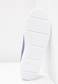 Baskets bleu marine avec une tige texturée, semelle en caoutchouc blanc avec des rainures horizontales et un logo en relief sur le côté.