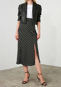 Falda midi negra con lunares, con abertura lateral, combinada con una chaqueta negra ajustada y una camiseta blanca; modelo lleva tacones negros con tiras.
