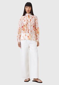 Bloemmotieven, lichtgewicht blouse met een hoge hals en gathers; gecombineerd met witte wijde broek en zilveren sandalen.