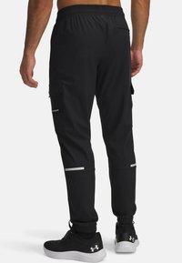 Zwarte sportbroek met een elastische tailleband, cargozakken, reflecterende accenten en taps toelopende boorden. Gemaakt van een lichtgewicht, rekbare stof.
