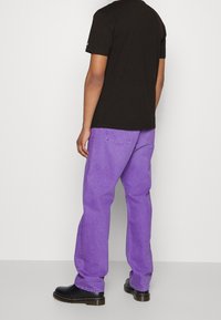 T-shirt noir à manches courtes associé à un pantalon en denim violet taille haute à coupe ample et des bottines noires. Textures textiles lisses.