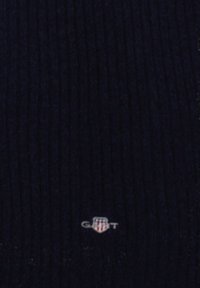 Tessuto a maglia a coste blu navy con una texture sottile. Piccolo logo in basso che indica il nome del marchio. Materiale morbido ed elastico.