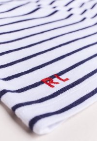 Weißer Stoff mit marineblauen Streifen, ausgestattet mit einem roten gestickten "RL" am unteren Rand. Weiche Textur, lässiges Design, geeignet für entspannte Kleidung.