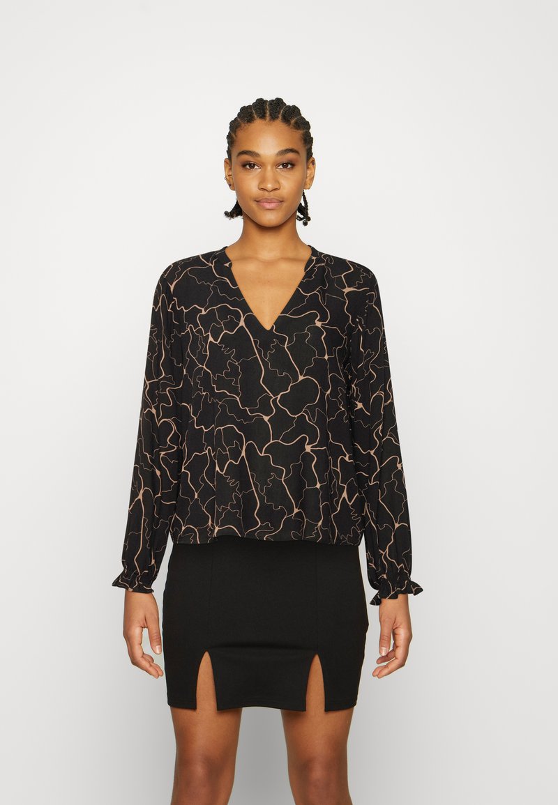 Blusa preta de manga longa com decote em V e padrão abstrato em linhas douradas, combinada com uma saia preta com duas fendas frontais.