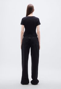 Μαύρο κοντό τοπ με κυματιστά άκρα σε συνδυασμό με άνετο μαύρο τζιν, με λεία υφή και δύο πίσω τσέπες.