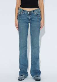 Světlé modré zvonové džíny vyrobené z denimu, s klasickým pětipocket designem, zapínáním na knoflík a mírným vyblednutím na nohách.