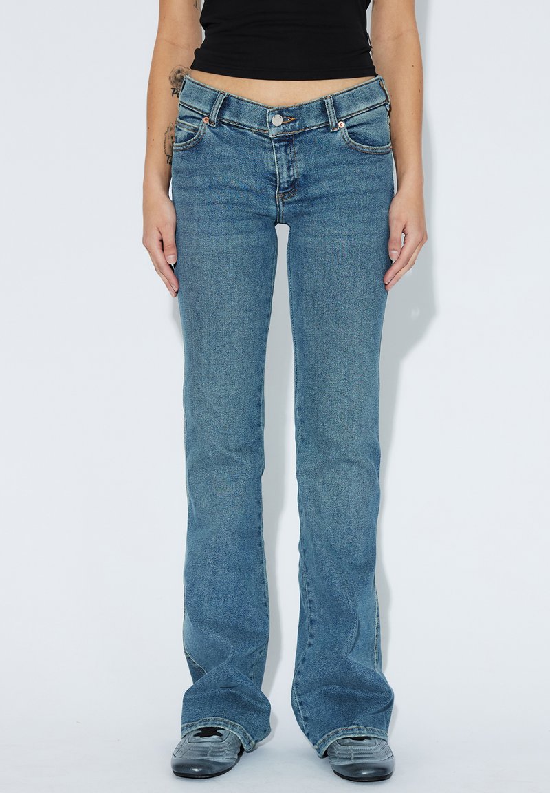 Světlé modré zvonové džíny vyrobené z denimu, s klasickým pětipocket designem, zapínáním na knoflík a mírným vyblednutím na nohách.