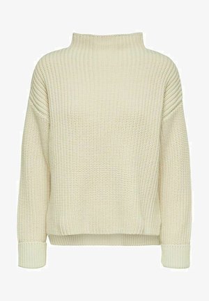 Dikke gebreide coltrui in romig beige. Geribbelde textuur met verlaagde schouders, losse pasvorm en omslagmouwen.