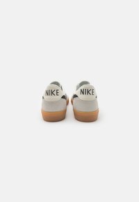 Αθλητικά παπούτσια Nike με γκρι σουέτ επάνω μέρος, μαύρες λεπτομέρειες, λευκά καπάκια φτέρνας και σόλα από καουτσούκ γάλακτος. Διαθέτουν έντονη σήμανση στο πίσω μέρος.
