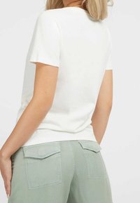 Camiseta blanca de manga corta hecha de algodón suave, diseño ajustado con cuello redondo, combinada con pantalones verdes claros de corte holgado que cuentan con bolsillos traseros.