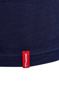 Marinblått tyg med ribbad textur, med en röd etikett märkt "hummel" sydd vid fållen. Rena linjer och prydliga sömnadsdetaljer.