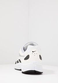 Bílé a šedé tenisky s texturovaným síťovaným svrškem, černými akcenty, polstrovaným límcem a tlustou bílou podrážkou. Výrazné logo a ventilační otvory.