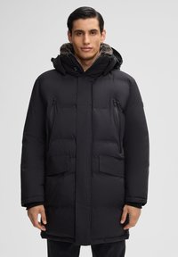 Zwarte gewatteerde winterjas met een bontgevoerde capuchon, twee met ritssluiting verpakte borstzakken en twee voorzakken met klep. Duurzaam materiaal met een gladde textuur.