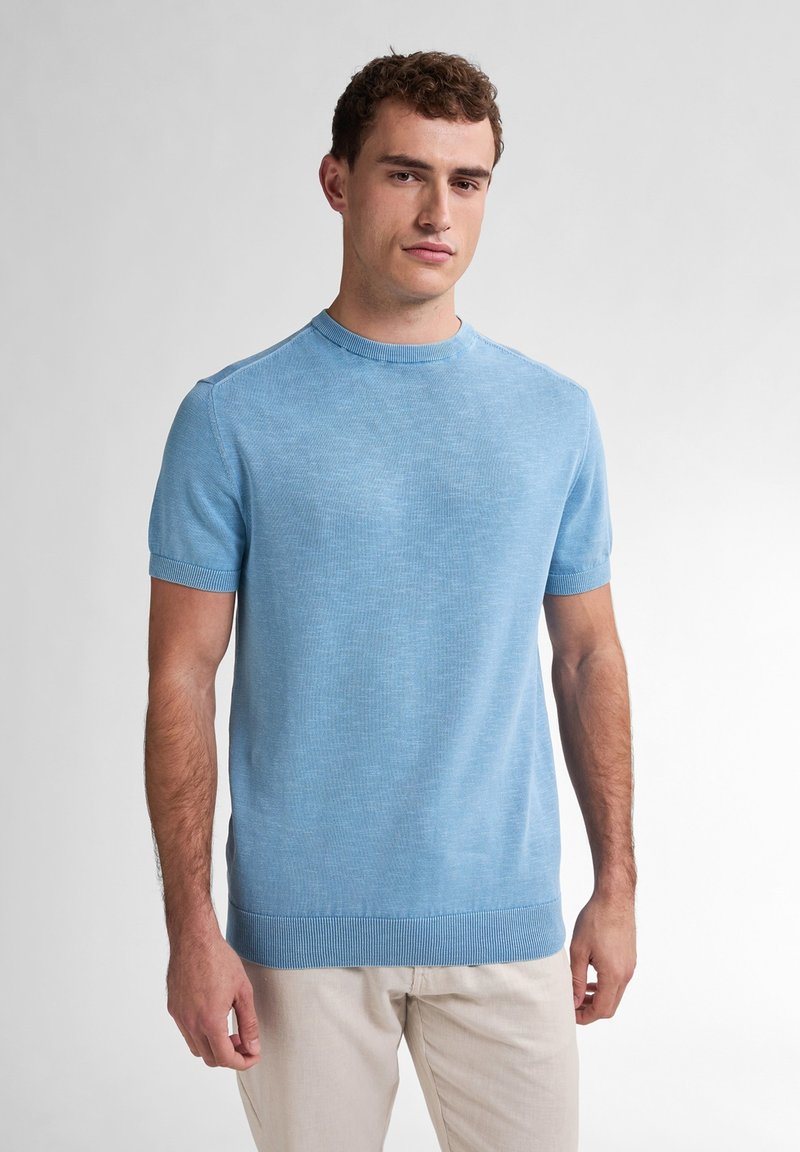 Pulover scurt, cu mânecă scurtă, de culoare albastru deschis, cu guler rotund, manșete și tiv ondulate. Textură fină cu un model uniform, subtil de tricot.