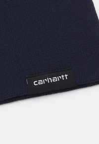 Marineblå strikket hue med ribbet tekstur, der har et sort mærke med hvid "carhartt" logo tydeligt vist på siden.