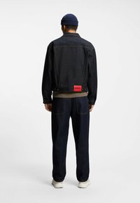 Dunkelblaue Jeansjacke mit rotem Etikett, kombiniert mit einem grün gerippten Pullover und dunkelblauen Hosen. Einfaches Design; glatte Textur.