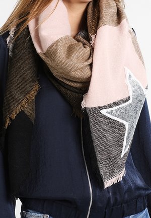 Femme portant une grande écharpe bicolore marron et rose avec une étoile argentée à paillettes, portée sur une veste bleu marine foncé à fermeture éclair avant.