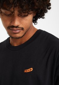 Zwarte katoenen T-shirt met een ronde hals en een klein oranje geborduurd "Volcom" logo aan de linkerkant van de borst.