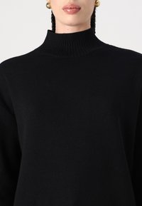 Fekete garbó pulóver ribbelt nyakkivágással és puha textúrával; laza szabással és hosszú ujjaival rendelkezik, ami kényelmes siluettet kölcsönöz.