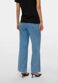 Jeans de pierna ancha en azul claro con un lavado medio, con dos bolsillos traseros, combinados con unos tacones negros de lunares.