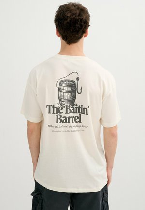 Hombre vistiendo camiseta blanca con gráfico de anzuelo y barril de pesca y texto "The Baitin' Barrel" en la espalda.