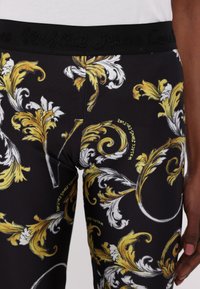 Leggings neri con un audace motivo floreale giallo e bianco, materiale elastico e una vita testurizzata con logo impresso.
