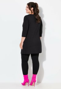 Tunica nera a tre quarti abbinata a leggings neri e stivaletti rosa shocking, che mette in mostra una texture liscia e un design aderente.