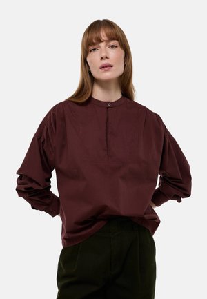 Blouse rayée bordeaux avec un col rond, patte de boutonnage sur le devant et manches longues surdimensionnées, assortie à un pantalon vert foncé.