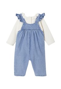 Hellblaue Denim-Latzhose mit Rüschendetails an den Schultern, kombiniert mit einem weißen Langarmoberteil mit Spitzenhalsausschnitt und geripptem Material.