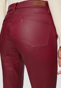 Burgundowe spodnie z faux skóry o gładkiej teksturze, z tylną kieszenią i przeszytą metką w pasie. Dopasowany krój podkreśla kształt.