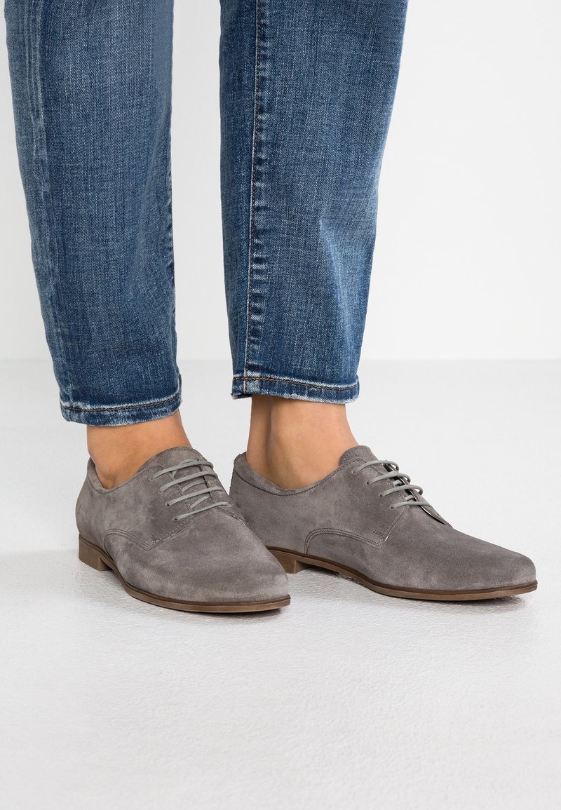 Chaussures à lacets en daim gris avec un bout rond, un talon bas et une surface texturée, associées à un jean bleu retroussé.