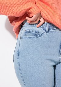 Světlé modré džíny z denimu s vysokým pasem a kapsami, ve spojení s texturovaným korálovým svetrem. Tkanina má mírný elastický efekt.