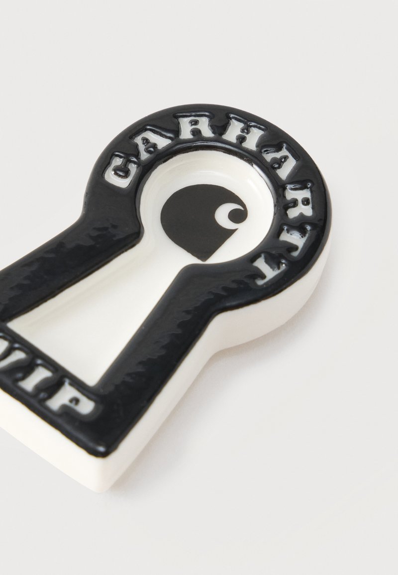 Schwarz-weiße Keramikschale in Form eines Schlüssellochs mit dem Wort „CARHARTT“, das rund um den oberen Rand geprägt ist.
