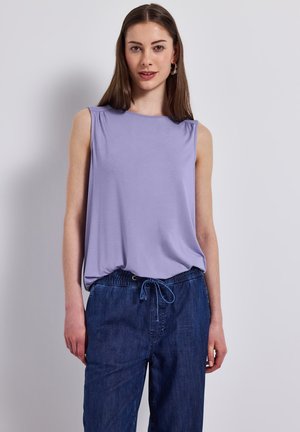 Haut sans manches violet avec une coupe décontractée, en tissu doux et avec des détails subtils aux épaules, associé à un pantalon en denim bleu foncé élastiqué.