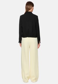 Schwarzer, kurzer Blazer mit langen Ärmeln, elastischem Taillenbund und glatter Textur, kombiniert mit weit geschnittenen, cremefarbenen Hosen.