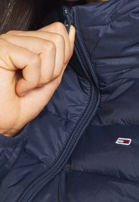 Navy puffjacka i närbild med dragkedjedetalj och logotyp, med kviltad textur och en mjuk, slät tygfinish.