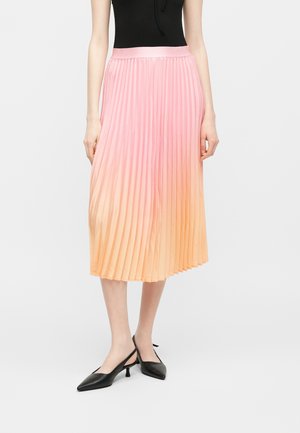 Femme portant une jupe midi plissée avec un dégradé ombré du rose à l'orange, associée à un haut sans manches noir et des chaussures noires à talons bas.