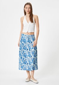Vit texturerad halterneck croptop tillsammans med en maxi kjol i blått med blommönster, med en ljusblå bakgrund och mörkblå blommor.