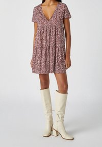 Vestido rojo con flores, con escote en V y mangas cortas, que presenta tejido fruncido y una silueta acampanada. Combinado con botas altas color crema hasta la rodilla.
