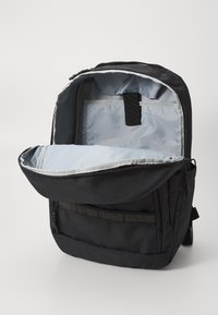 Mochila negra con el compartimento principal abierto, mostrando un interior gris claro y una funda acolchada para un portátil o tableta.