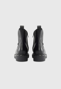 Bottes chevilles en cuir noir avec une texture lisse, des zips sur les côtés et une semelle épaisse et texturée. Talon bas et pattes de tirage pour un enfilage facile.