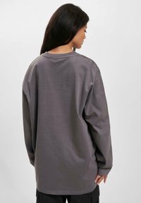 Long-sleeve shirt in dark gray, made of soft fabric with a relaxed fit, rounded neckline, and dropped shoulder seams, featuring minimal stitching.