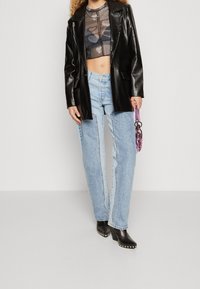 Blazer de cuero sintético negro sobre un top corto transparente con estampado, jeans de tiro alto en azul claro y botines negros de tacón con tachuelas.