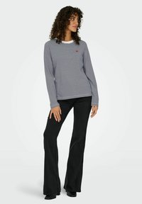 Langarm gestreept shirt in marineblauw en wit met een ronde hals, voorzien van een klein rood logo op de borst. Gepaard met zwarte flared jeans.