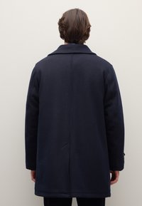 Abrigo de lana azul marino con una silueta clásica, cuello con muesca y detalles de botones en los puños. Presenta un corte recto y textura suave.