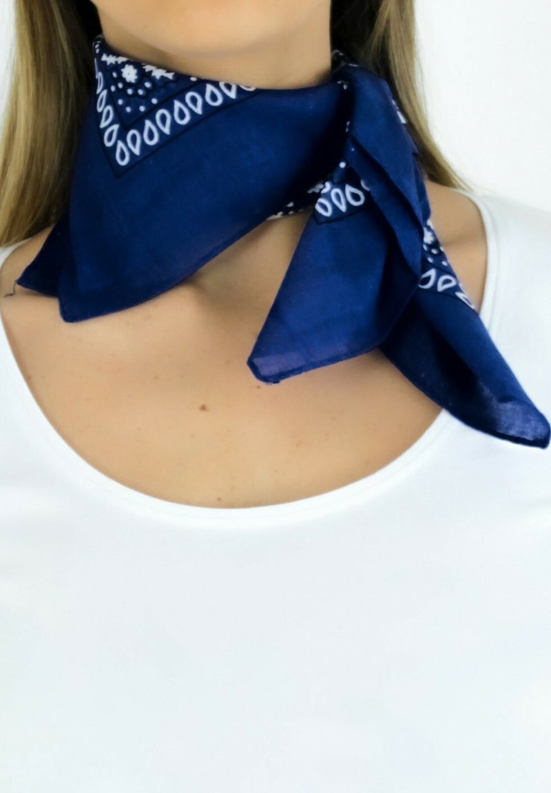 Foulard en soie bleu marine avec un motif paisley sur les bordures, noué autour du cou, tombant doucement sur une chemise blanche.