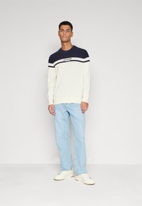Felpa con colletto rotondo caratterizzata da una parte superiore blu navy, una parte inferiore bianca e strisce orizzontali con logo. Abbina a jeans azzurri chiari e scarpe bianche.
