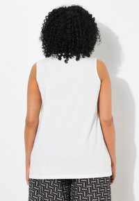 Bílý bez rukávů top s hladkým povrchem a kulatým výstřihem. Doplněný o kalhoty s černým cik-cak vzorem, které mají elastický pas.